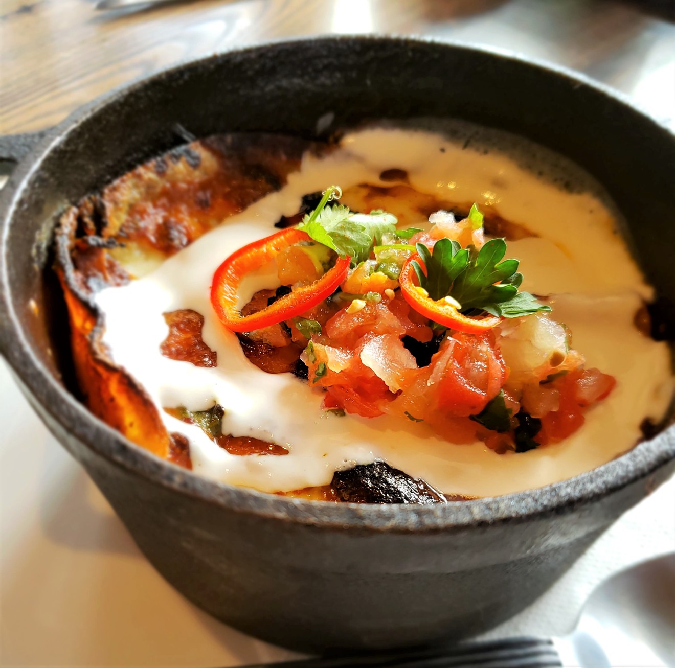 The Ghost Ranch Aztec Cake is layered tortillas, pulled chicken, roasted green chile, sweet corn, and cheese topped with crema and garnish, served in a cast-iron skillet.