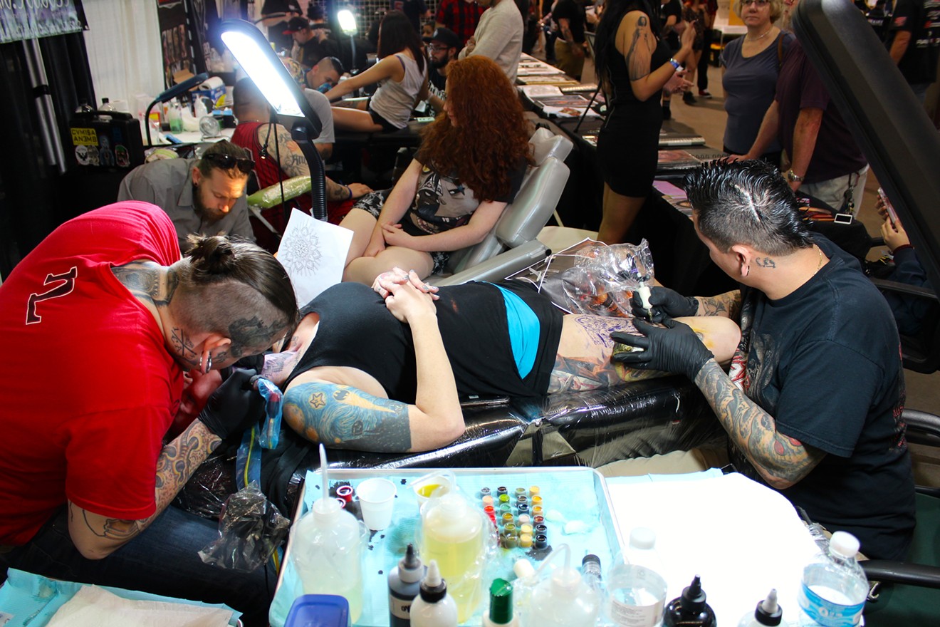 A brave patron at the Phoenix Body Art Expo opts to get two tattoos at once on the front of the neck and inner thigh. Both skin spaces are sensitive areas.