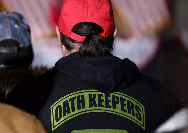 Image: a person seen from behind in a red hat and "oath keepers" sweatshirt