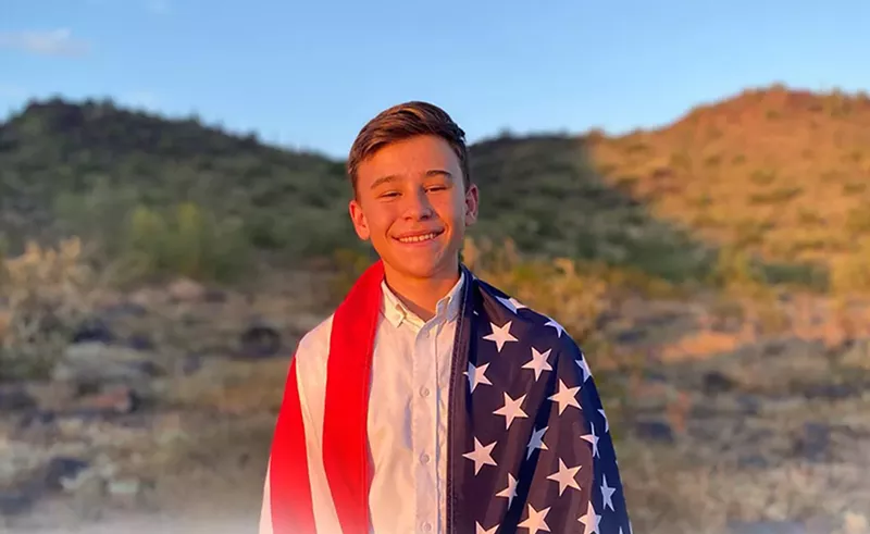 Image: a baby-faced teen boy draped in an American flag