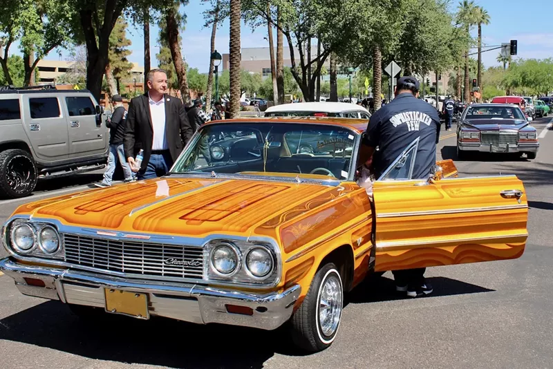 Image: Two people get out of an orange lowrider car.