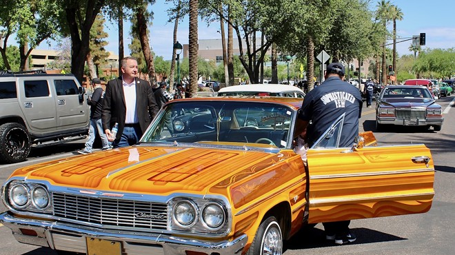 Two people get out of an orange lowrider car.