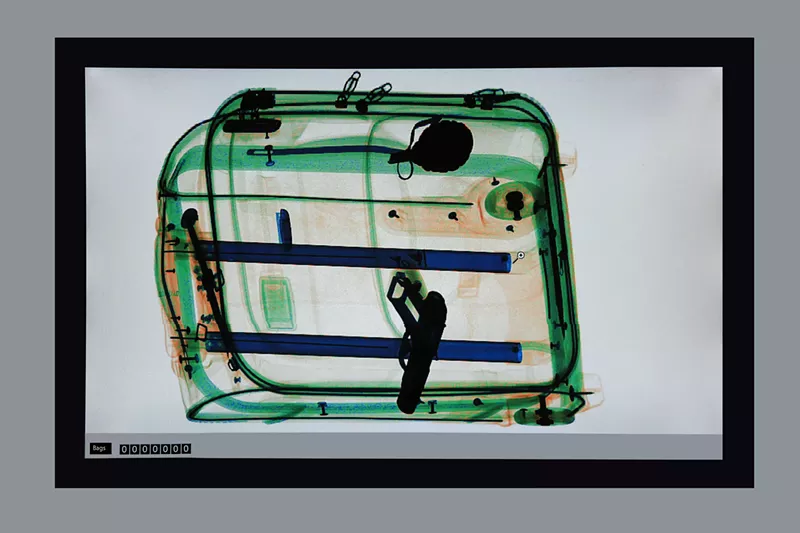 Image: an x-ray of a suitcase showing a handgun in it