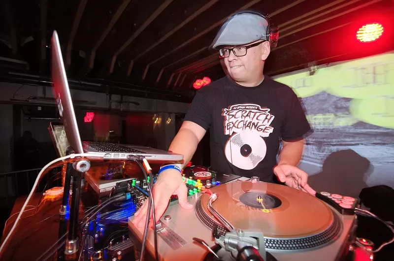 Image: A Filipino man DJs on a pair of turntables in a nightclub.