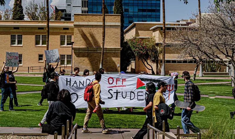 Image: students hold up a banner that says "hands off our students" on asu's campus