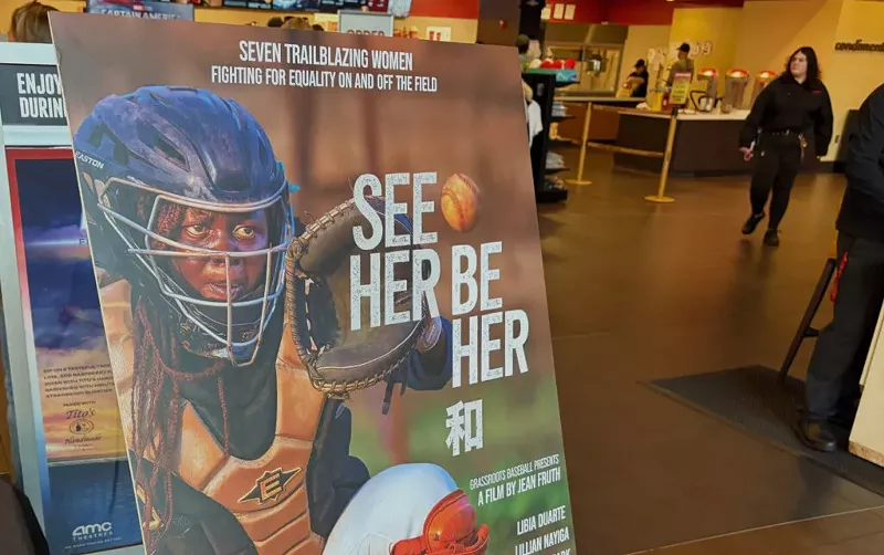 Image: The promotional poster for “See Her Be Her” is showcased in the lobby of Desert Ridge AMC Theatres in Phoenix. The documentary highlights the impact on women’s baseball.
