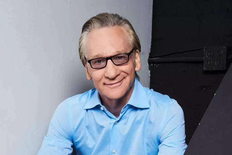 Image: Bill Maher wearing a blue shirt and glasses.