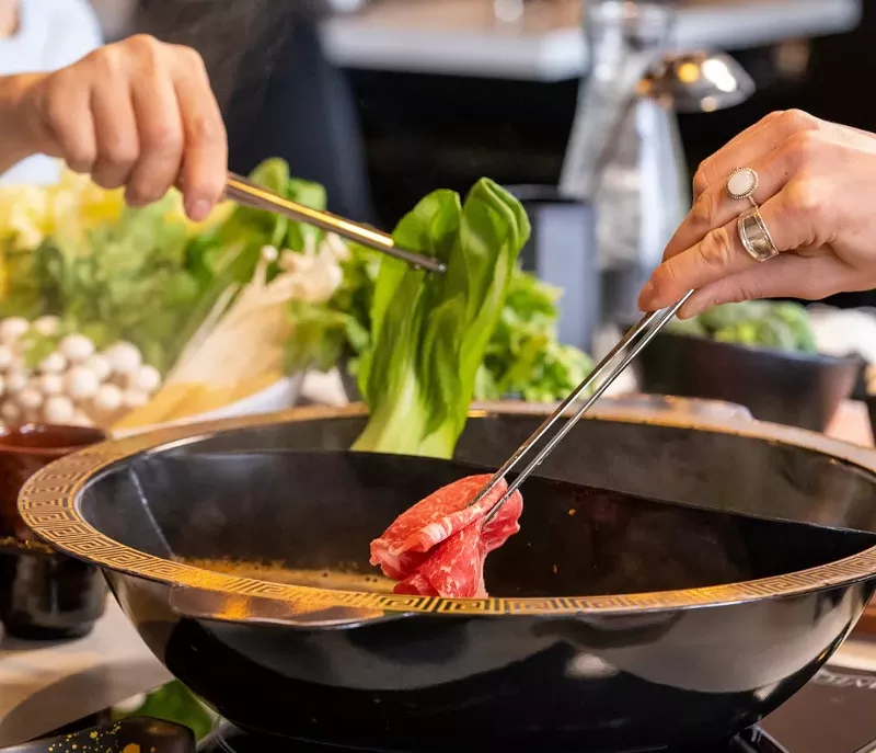 Image: Dipping meat and vegetables into a hot pot.