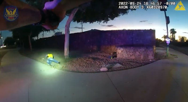 Image: body-cam footage showing hands pointing a gun at a figure in a yellow shirt on the ground