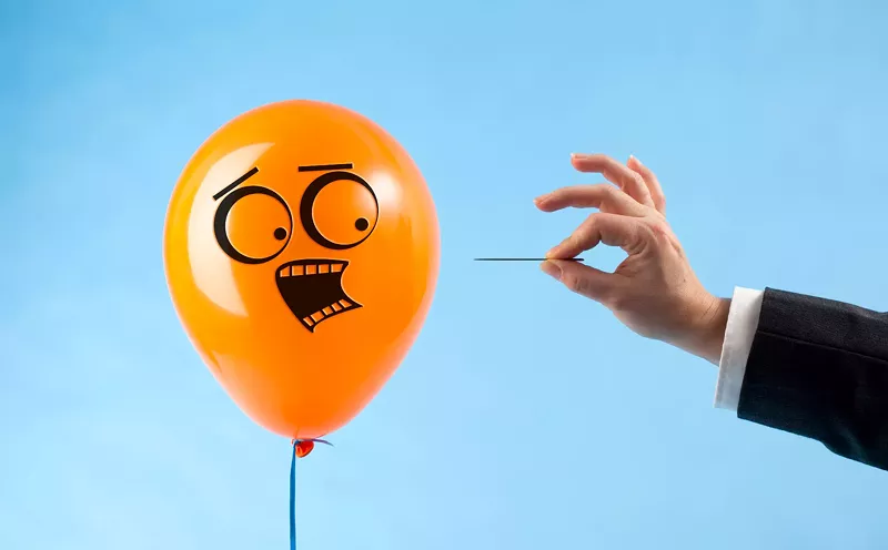Image: a balloon with a scared face looks at a hand with a pin