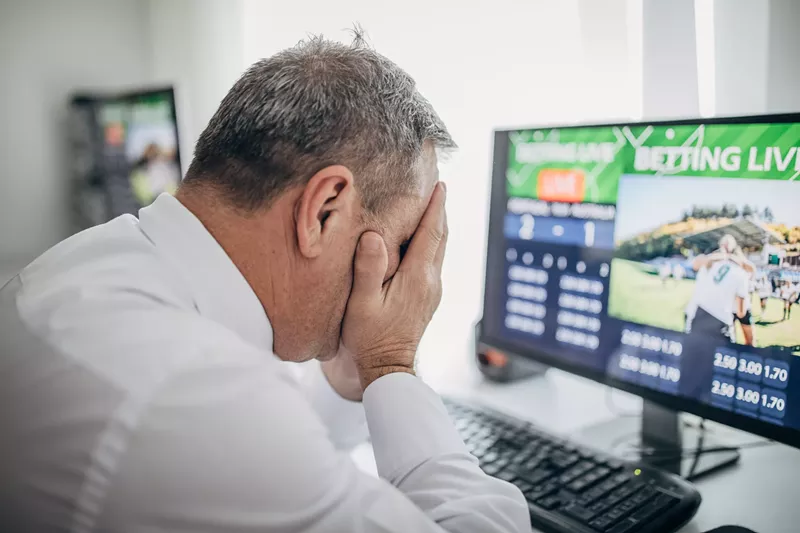Image: a man puts his head in his hands while looking at a computer screen