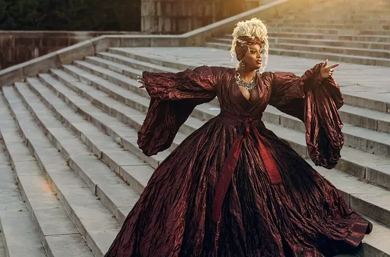 Image: A drag queen in a ballgown on the steps of a palace.
