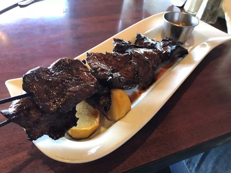 Image: Beef hearts deeply scored and leaking juice on a hot metal skewer.