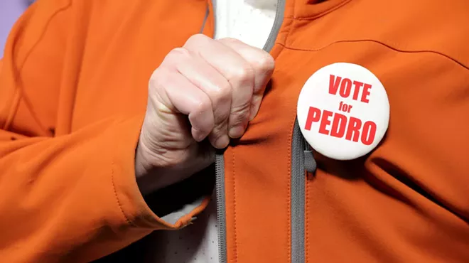 a hand grabs the lapel of an orange jacket that features a "vote for pedro" pin