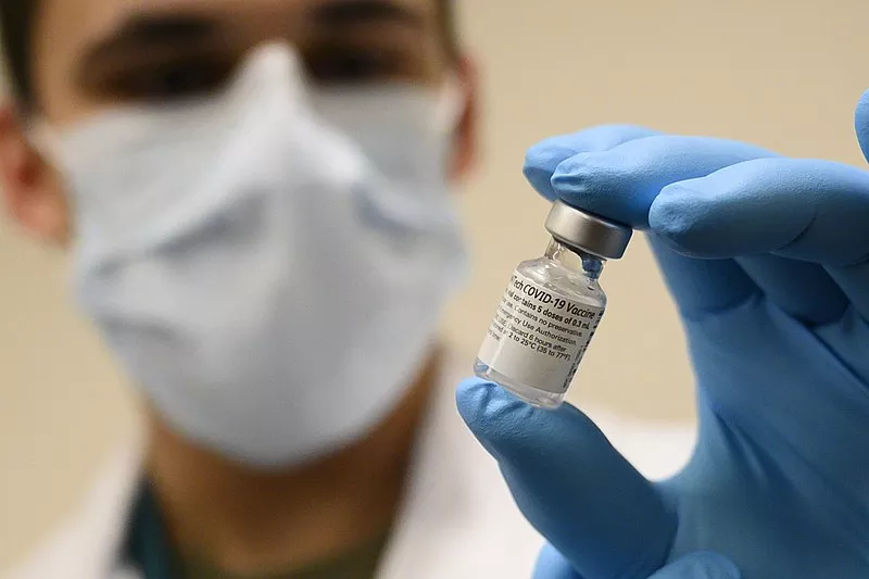 Image: a masked medical worker holds a vial of covid-19 vaccine