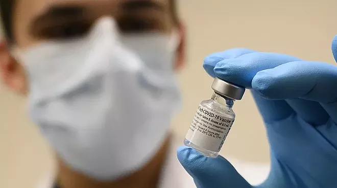 a masked medical worker holds a vial of covid-19 vaccine