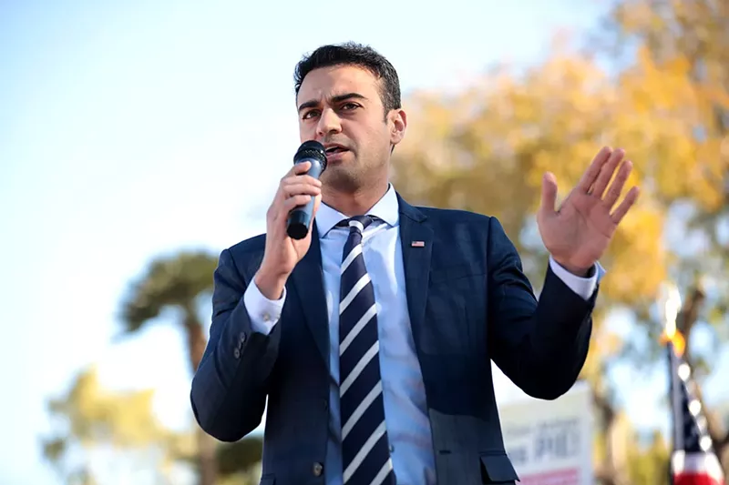 Image: A man in a suit and tie speaking into a microphone outdoors