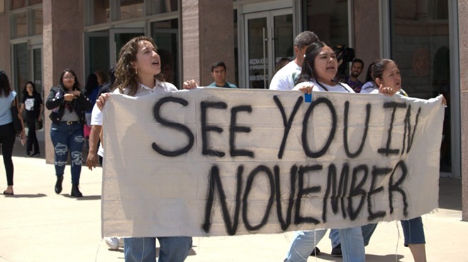 Three people march holding a banner that says, "See you in November"