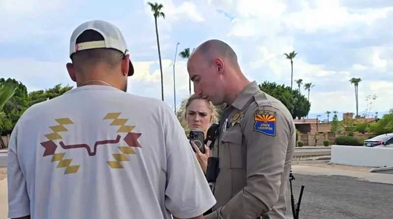 Image: an Arizona Department of Public Safety trooper speaks to a man in a white shirt and hat