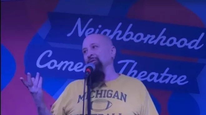 a man in a michigan football shirt on stage at a comedy club
