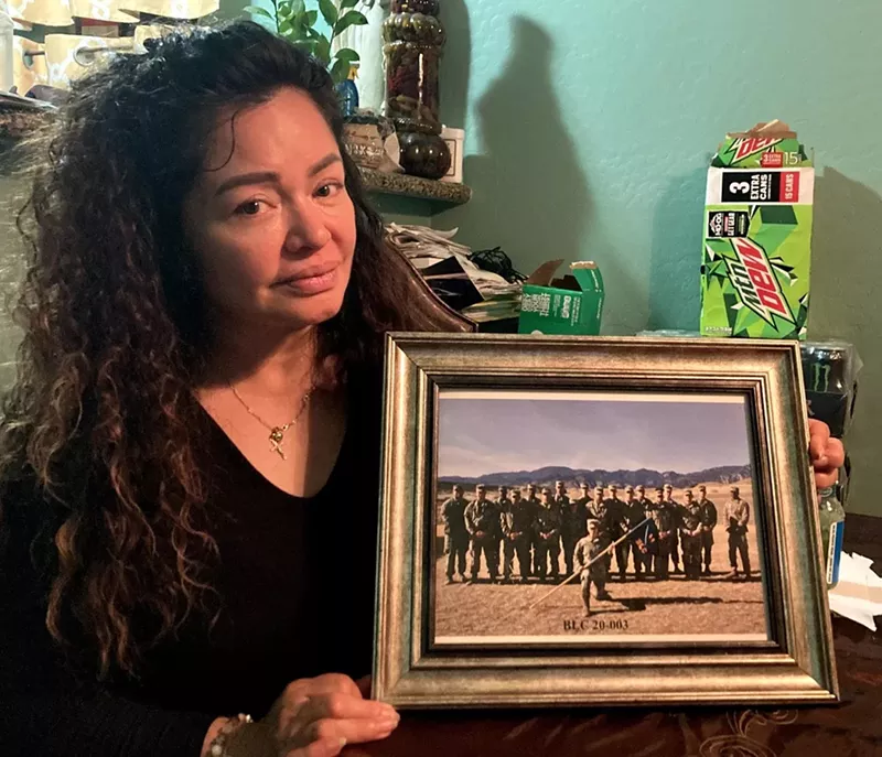 Image: A woman holds a framed photo of soldiers.