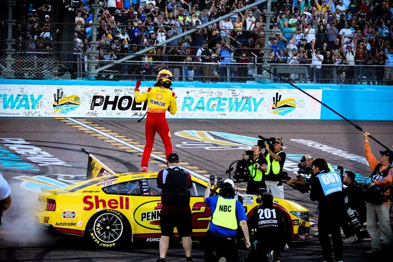 Image: A racecar driver celebrates on a racetrack.