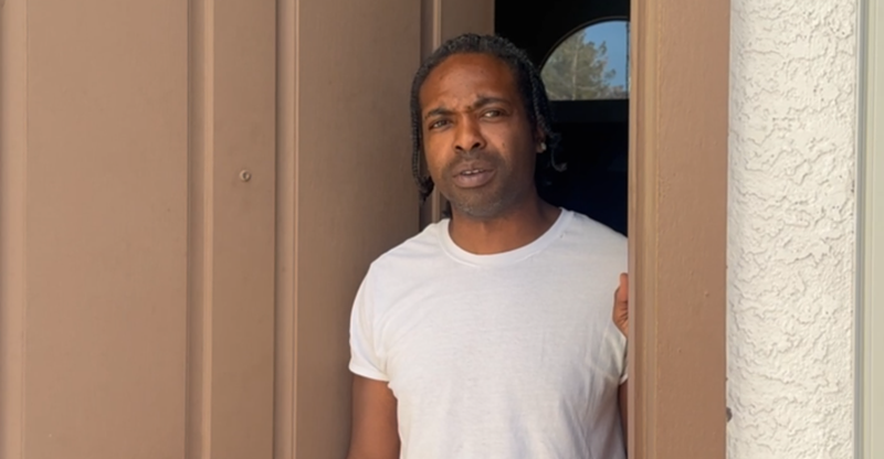 Image: a man in a white shirt standing in an open doorway