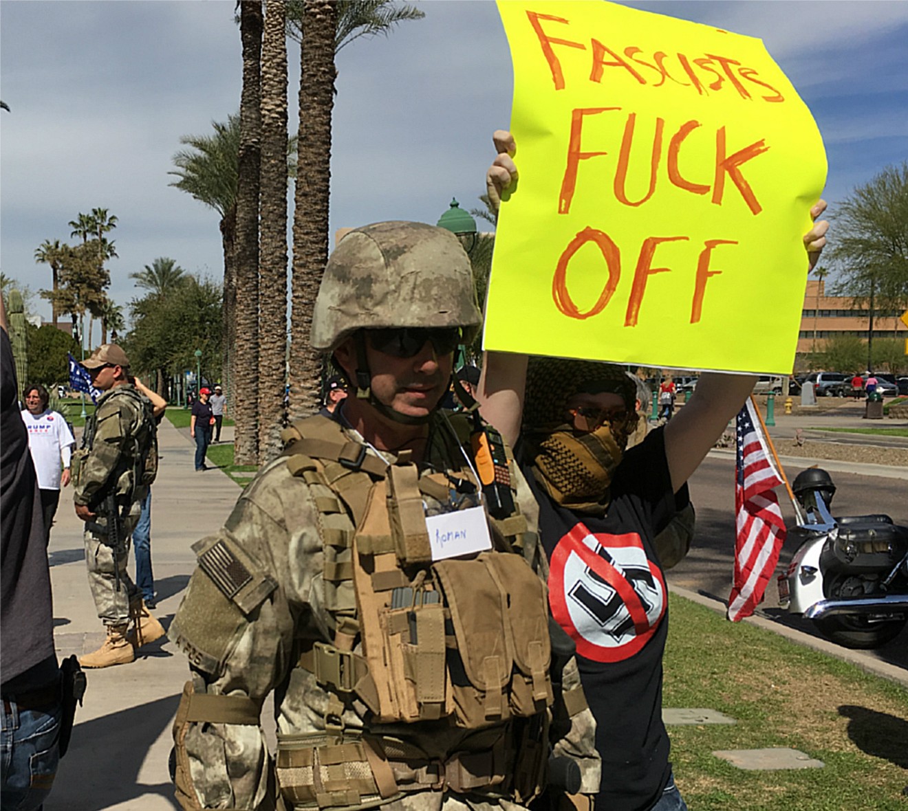 One of several heavily-armed militiamen (left) doing security at Saturday's March4Trump at the Arizona Capitol, while an antifascist gal demonstrates against the gathering.