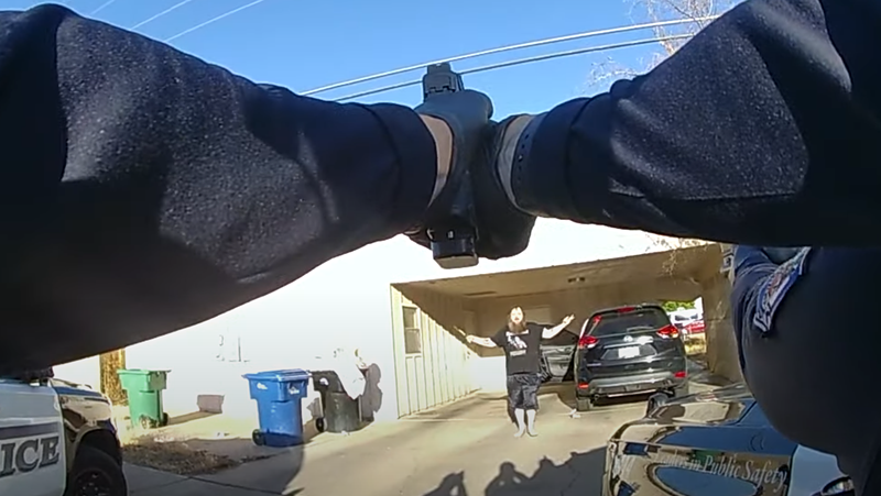 Image: body-cam footage showing hands holding out a gun at a man who has his arms raised and a knife in one hand