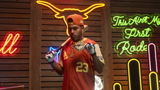 A man in a baseball jersey in front of a wall of neon signs.