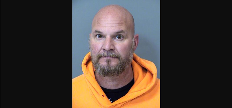Image: a bald man with a goatee in an orange hoodie seen in a mugshot