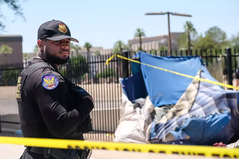 Image: A Phoenix police officer stands in front of a tent belonging to an unhoused person