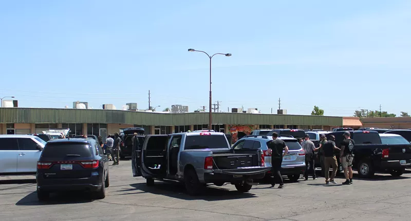 Image: a bunch of unmarked law enforcement vehicles in a parking lot, with people milling about