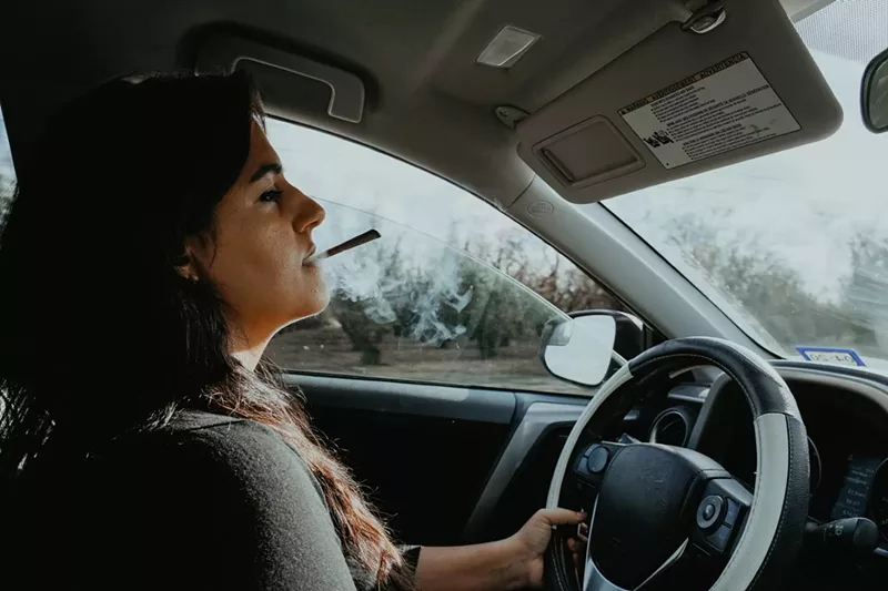 Image: a woman smoking a joint behind the wheel of a car