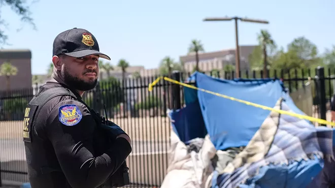 A Phoenix police officer stands in front of a tent belonging to an unhoused person
