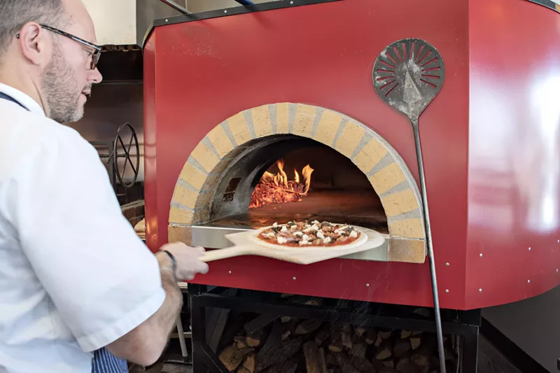 Image: Chef Tony Snyder at the brick oven with a Salsiccia pizza.
