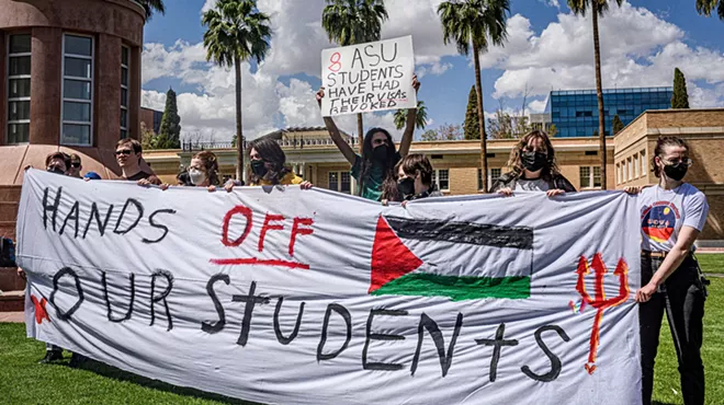 people hold a banner that says "hands off our students" with a Palestinian flag