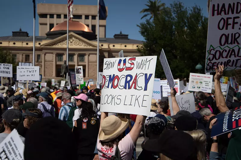 Image: protesters at the arizona capitol. one sign says "show us what democracy looks like"