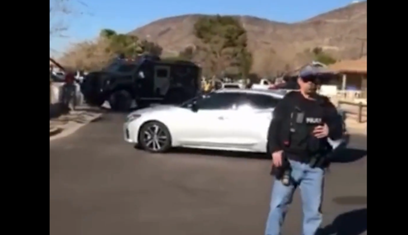 Image: an ICE agent with a rifle stands in front of an unmarked car and an armored truck