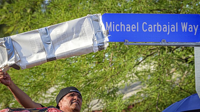 A man pulling a cover of a street sign that reads "Michael Carbajal Way"