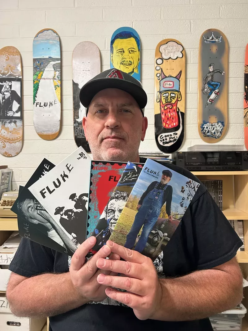 Image: A man in a hat holding up a selection of zines.