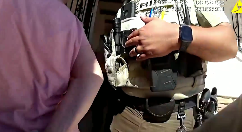 Image: body-cam footage showing a handcuffed old woman from behind next to a sheriff's deputy