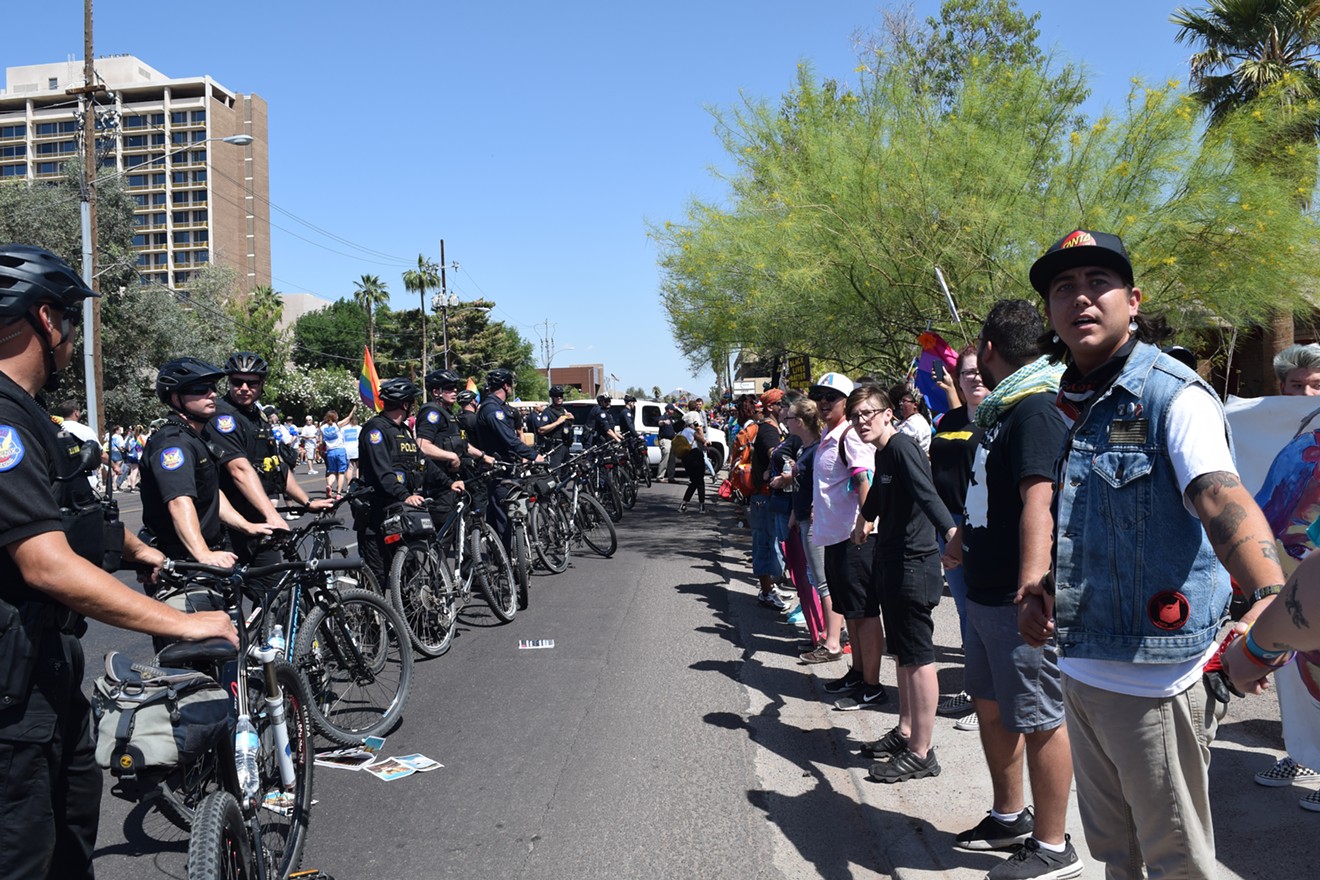 Phoenix police and LGBTQ migrant rights activists face off on the sidewalk. Demonstrators briefly blocked the parade route on Sunday before police pushed them to the curb.