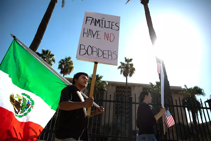 Image: a protester holds a mexican flag and a sign that says" families have no borders"