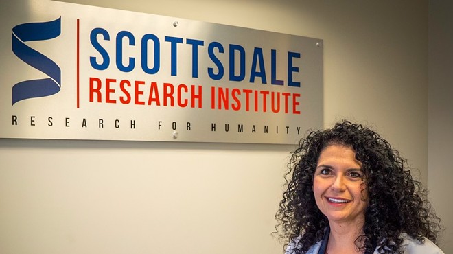 a woman in a lab coat stands in front of a sign for Scottsdale Research Institute