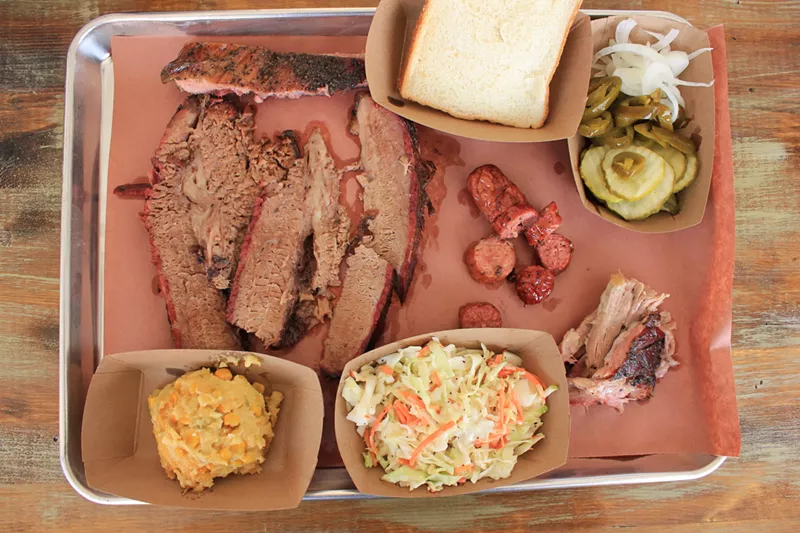 Image: A platter of brisket, sausage, pulled pork, a rib, and sides.
