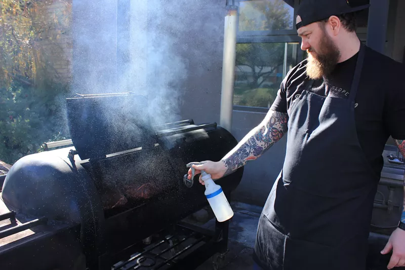 Image: Dom Ruggiero sprays pork shoulders in his 120-gallon smoker.