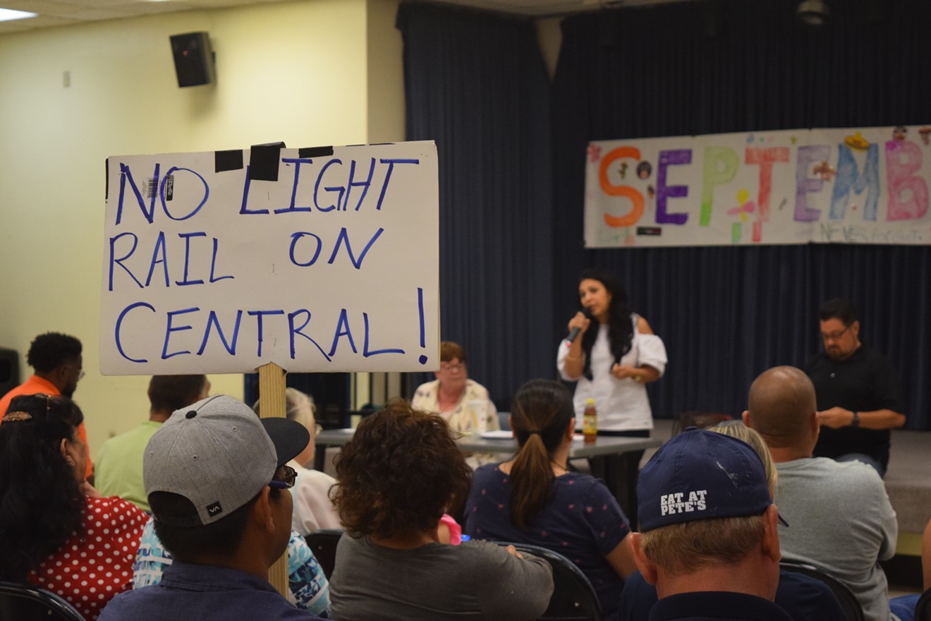 Eduardo Sanchez, 24, holds a sign at a community meeting on light rail on September 17. In the background, from left, are City Council members Debra Stark, Felicita Mendoza, and Michael Nowakowski.
