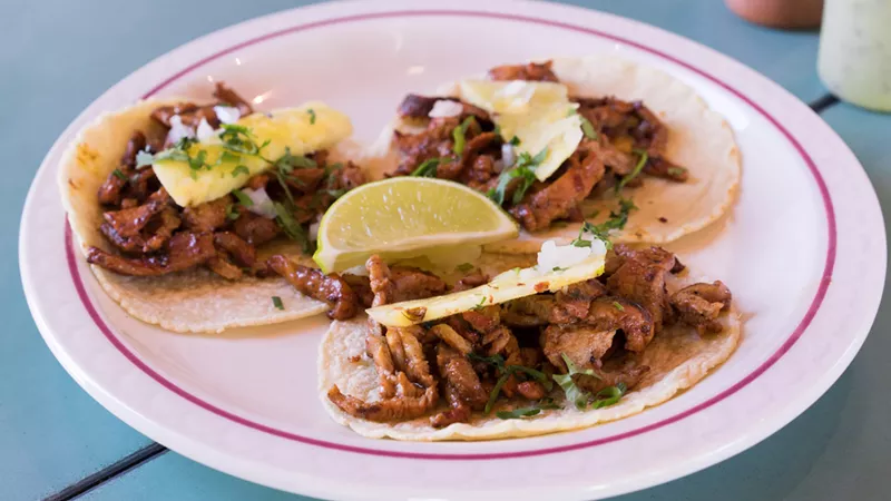 Image: Al pastor, grilled over a wood fire and then finished in a ripping hot wok, comes together atop tacos, topped with onion, cilantro, and a thin sliver of pineapple.