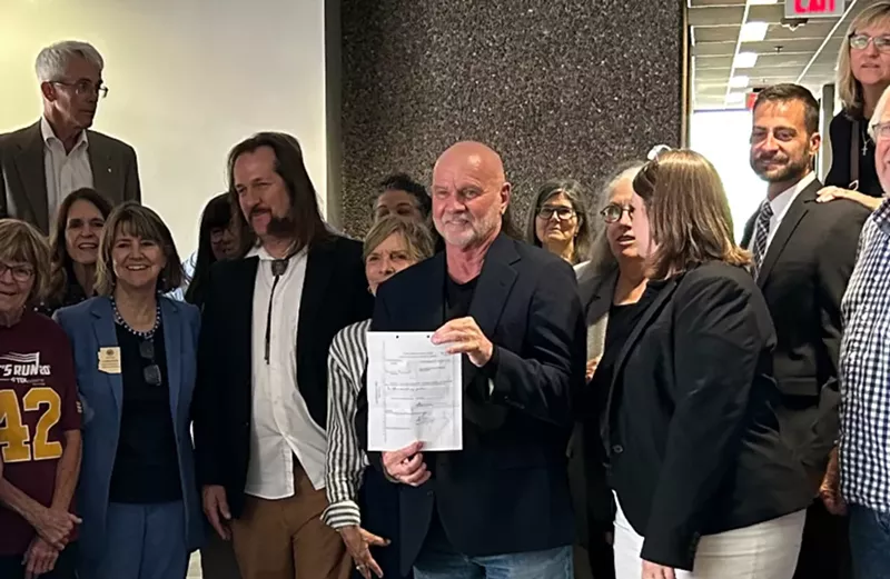 Image: a man holds up a sheet of paper surrounded by other people